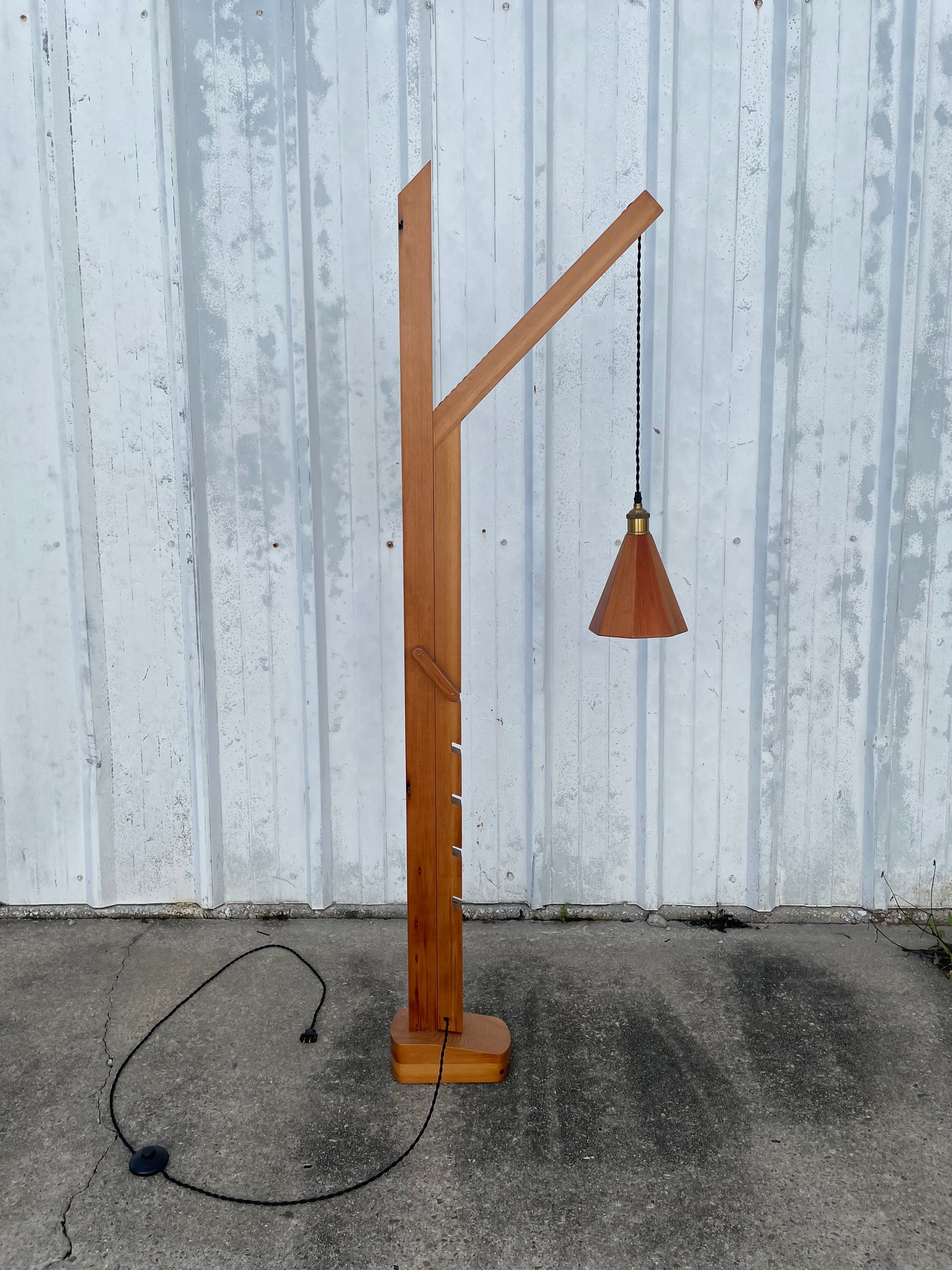 adjustable height Wooden lamp with a cone-shaped wwoden shade on a concrete surface with a cloth cord and footswitch 