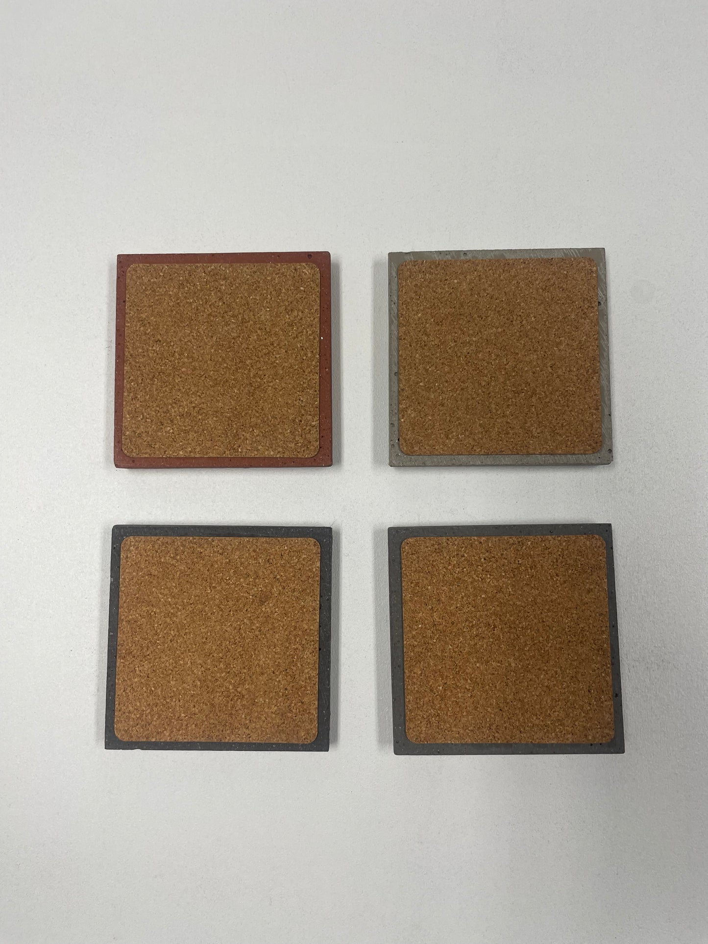 Set of 4 concrete coasters with cork backing in light grey, medium grey, dark grey, and red