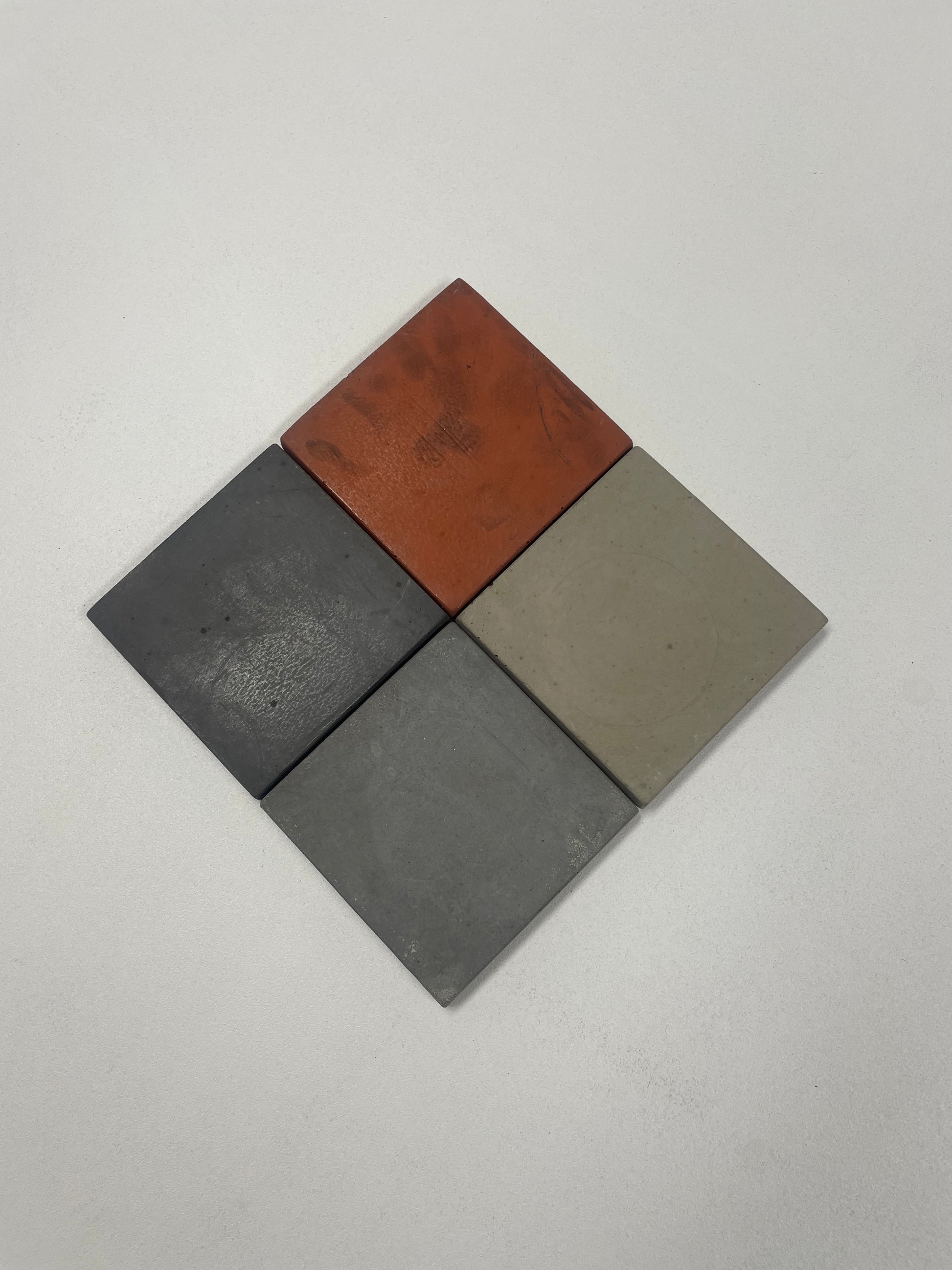 Set of 4 concrete coasters with cork backing in light grey, medium grey, dark grey, and red