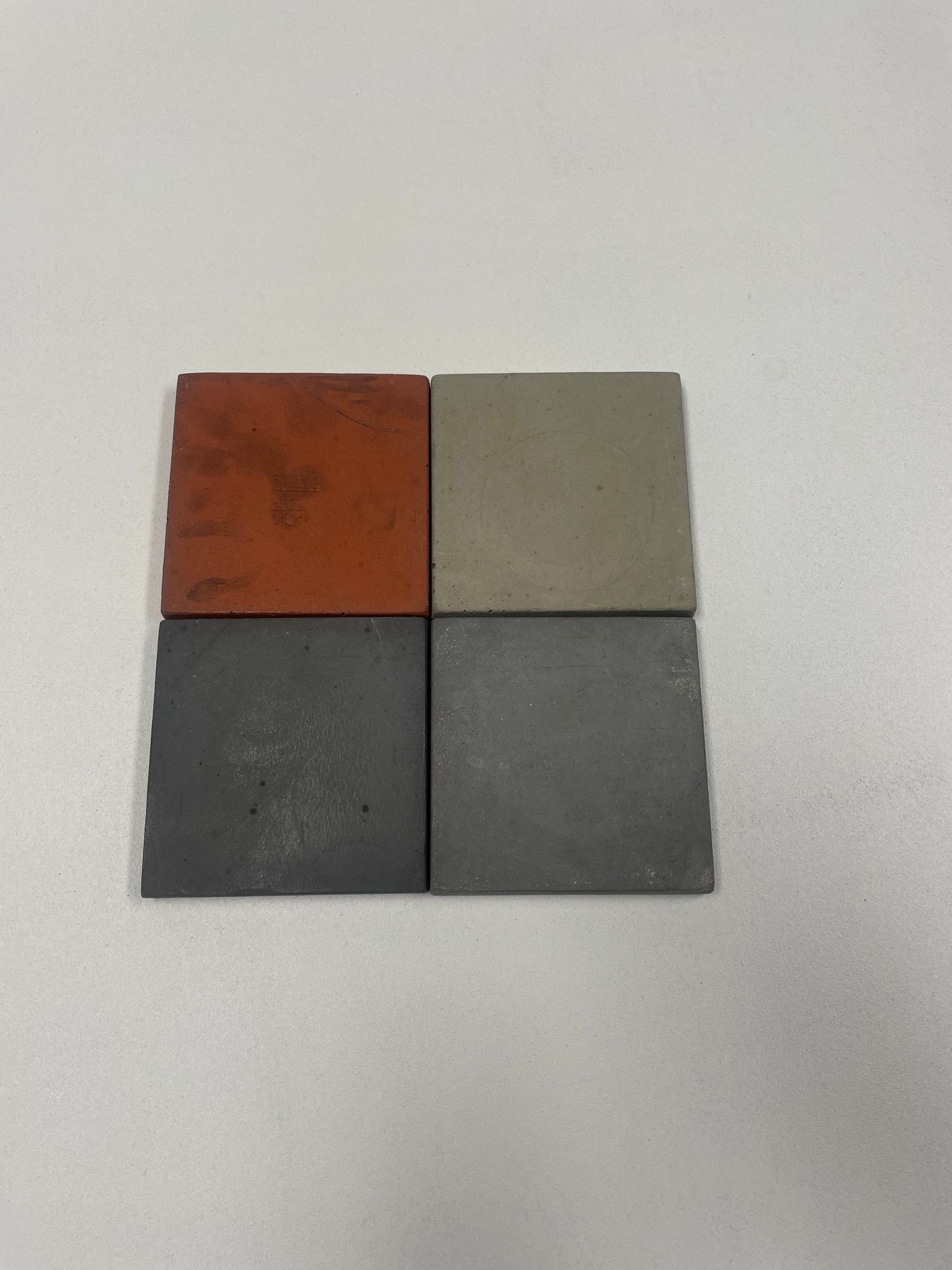 Set of 4 concrete coasters with cork backing in light grey, medium grey, dark grey, and red