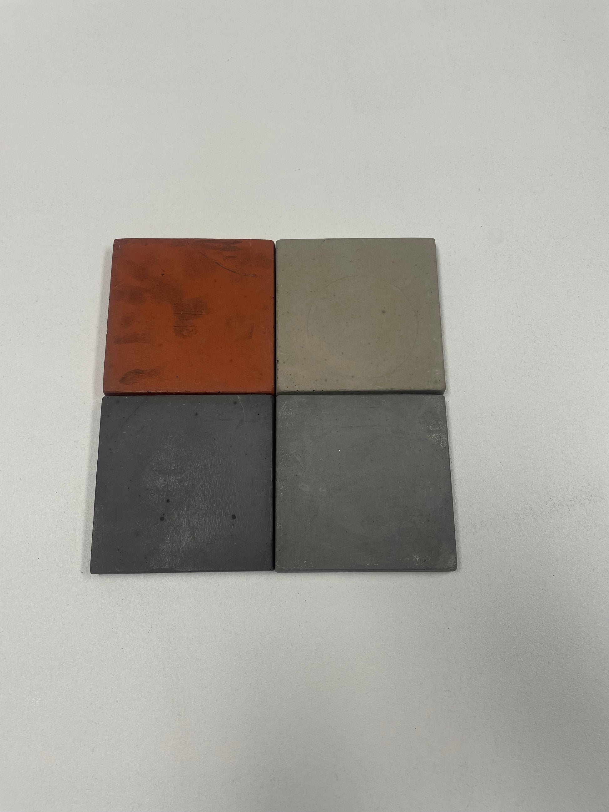Set of 4 concrete coasters with cork backing in light grey, medium grey, dark grey, and red